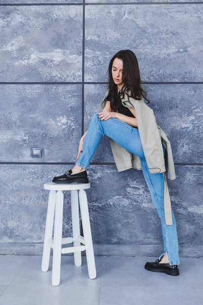 Hermosa mujer con piernas esbeltas en jeans y ropa de moda con un impermeable elegante zapatos de cuero Imagen de mujer en estilo primaveral