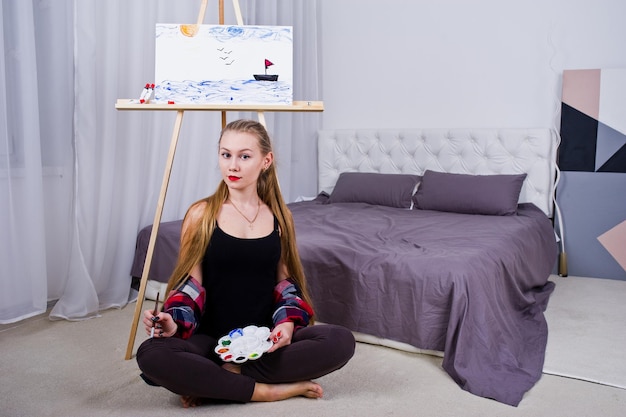 Hermosa mujer pintora con pinceles y lienzo al óleo posando en la cama en la habitación