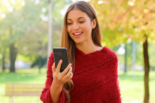Hermosa mujer con poncho rojo leyendo sms en su teléfono móvil al aire libre.