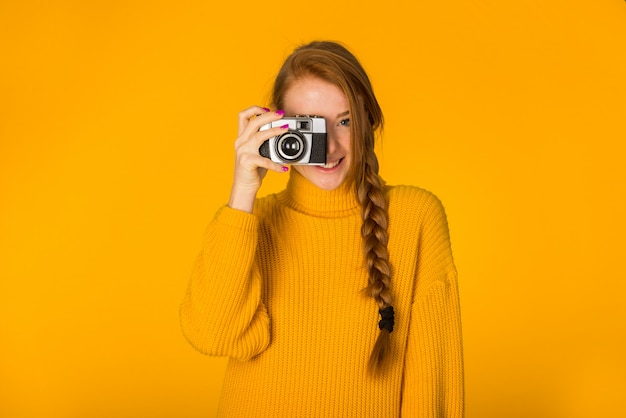Hermosa mujer posando con cámara en pared naranja