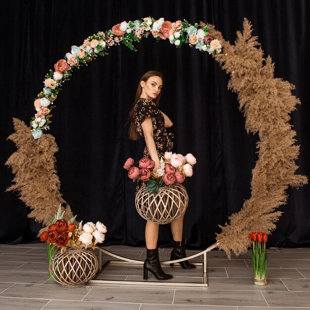 Hermosa mujer posando en el círculo de madera muerta en vestido con estampado de flores en estudio