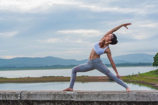 Hermosa mujer practicando yoga junto al lago con la montaña.