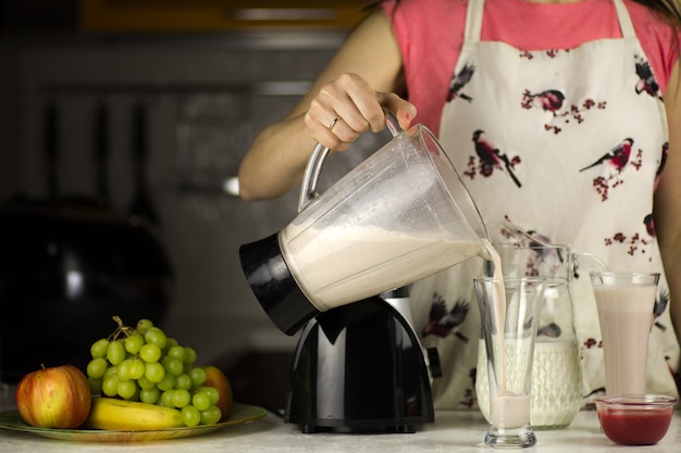 Una hermosa mujer preparando un cóctel de leche con frutas en la cocina