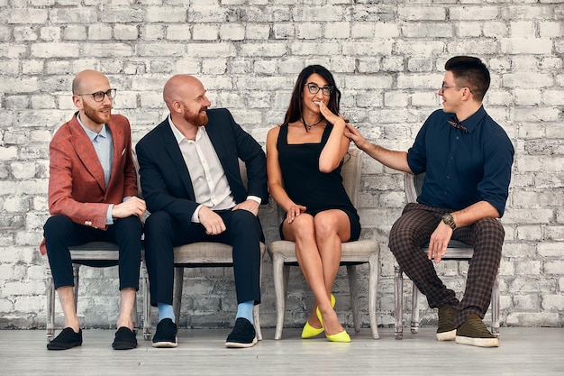 Hermosa mujer profesional alegre con gafas sentada con compañeros de trabajo masculinos y líder de equipo