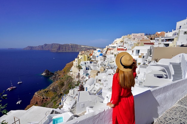 Hermosa mujer en el pueblo de Oia tiene sombrero cuando mira el paisaje urbano desde la terraza en la isla de Santorini Grecia