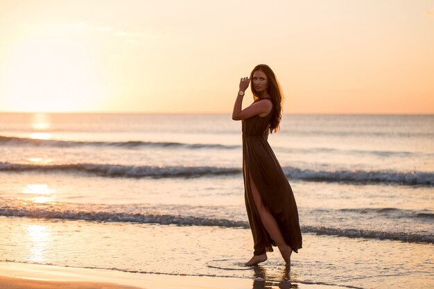 Hermosa mujer en puesta de sol. Colorido amanecer sobre el mar. Mujer despreocupada disfrutando del atardecer en la playa. Estilo de vida feliz