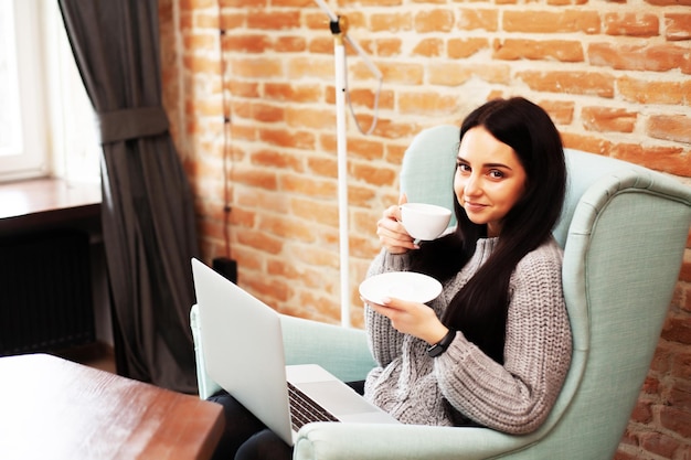 Hermosa mujer que se queda en casa y trabaja en la computadora portátil en línea.