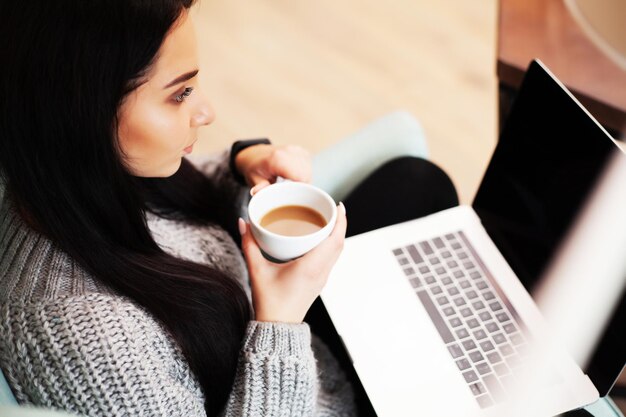 Hermosa mujer que se queda en casa y trabaja en la computadora portátil en línea.