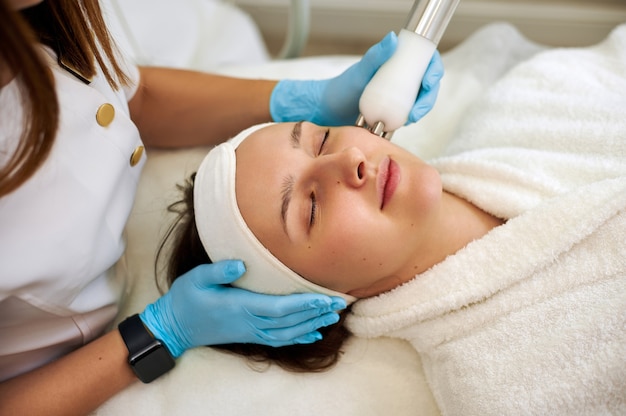 Hermosa mujer que recibe el procedimiento de microcorriente facial para levantar y rejuvenecer la piel.