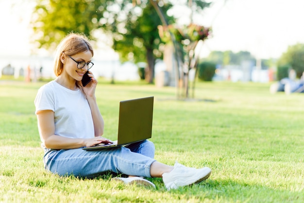 Hermosa mujer que trabaja con la computadora portátil en el parque sobre la hierba. El concepto de trabajo a distancia