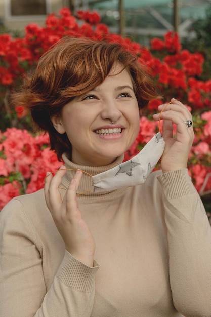 Foto una hermosa mujer se quita la máscara protectora y inhala entre las flores de primavera