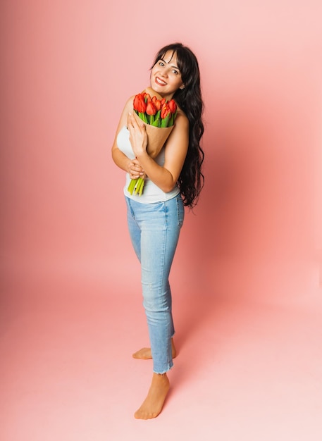 Hermosa mujer con un ramo de tulipanes de flores de primavera sobre un fondo rosa Concepto de día de la mujer de regalo