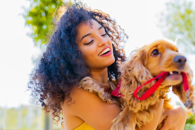 Hermosa mujer de raza mixta con maquillaje y peinado rizado pasando momentos felices con su perro cocker americano de oro citado en un día soleado en la calle