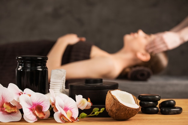 Hermosa mujer recibiendo masaje de cabeza en spa flores de orquídeas coco y piedras