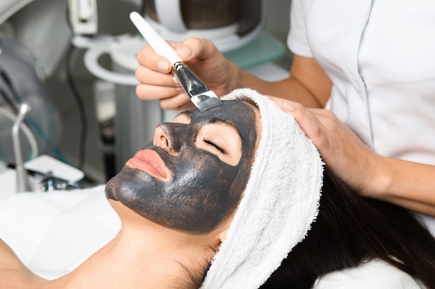 Hermosa mujer recibiendo mascarilla facial con efectos rejuvenecedores en el salón de belleza spa.