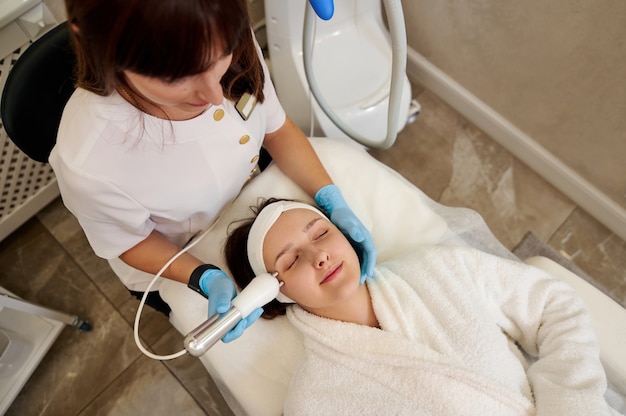 Foto hermosa mujer recibiendo tratamiento de microcorriente facial de esteticista en salón de belleza y bienestar. terapia de microcorrientes.