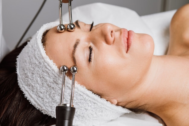 Hermosa mujer recibiendo tratamiento de microcorriente facial en el salón de spa. Esteticista utilizando impulsos eléctricos para procedimientos faciales.