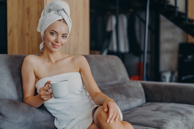 Foto hermosa mujer relajada envuelta en una toalla bebiendo té