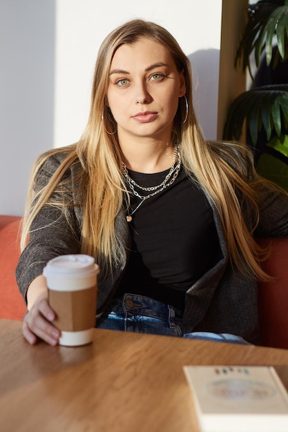 Hermosa mujer relajada vestida de negro sentada sola en un café con una taza de café desechable