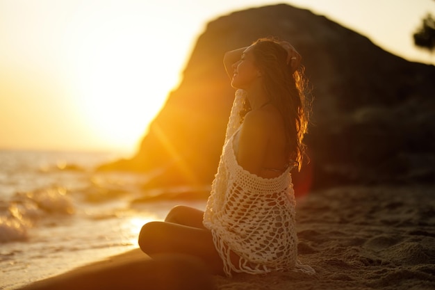 Hermosa mujer relajándose en la arena en la playa y disfrutando al atardecer