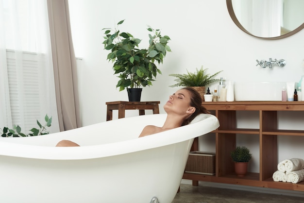 Foto hermosa mujer relajante en una tina de baño con los ojos cerrados en vista de perfil de felicidad y placer. mujer joven, relajante