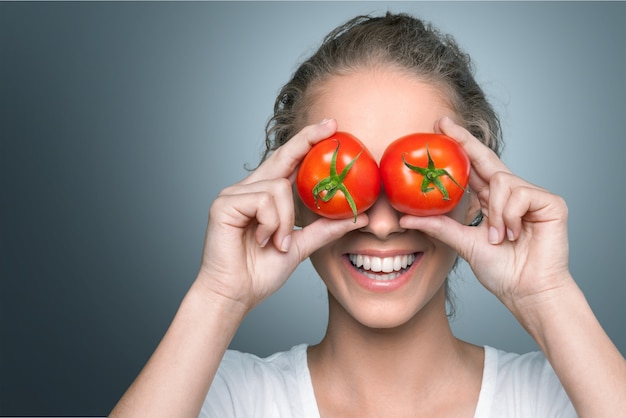 Hermosa mujer riendo sosteniendo dos tomates maduros ante sus ojos.