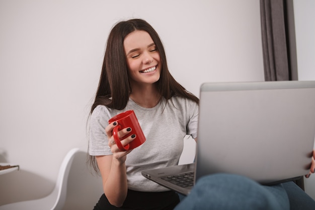 Hermosa mujer riendo, usando su computadora portátil para videollamadas, trabajando desde casa durante la cuarentena