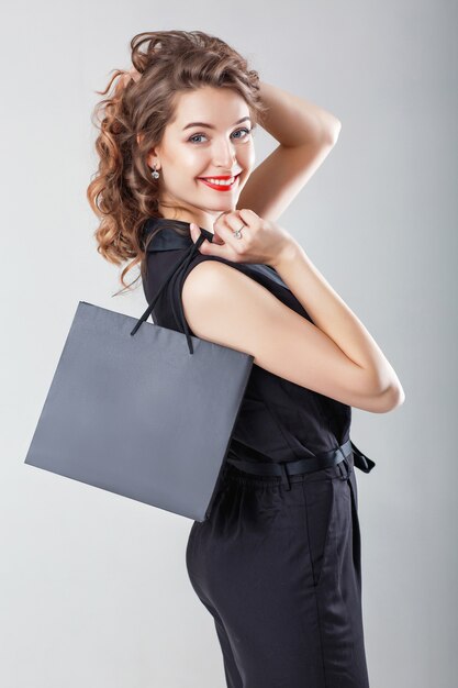 Hermosa mujer rizada feliz en negro elegante en general con bolsa de compras