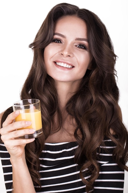 Hermosa mujer con rizos de cabello de piel saludable y jugo de naranja posando en el estudio