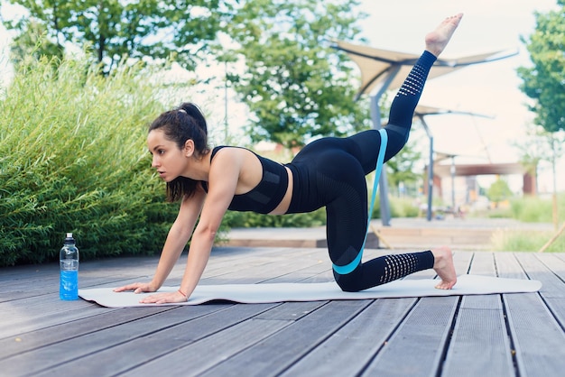 Hermosa mujer en ropa deportiva azul haciendo ejercicios de estiramiento con gomas de fitness en blanco