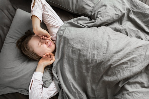 Hermosa mujer en ropa de dormir se estira en la cama en su casa y sonríe de un buen descanso. Sueño saludable Vista superior