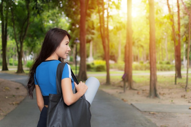 Hermosa mujer con ropa de entrenamiento azul sosteniendo una colchoneta enrollada en el parque por la noche Ella está feliz de ir al ejercicio