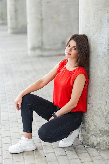 hermosa mujer con ropa de estilo informal sentada cerca de una columna gris en la calle. tiro al aire libre