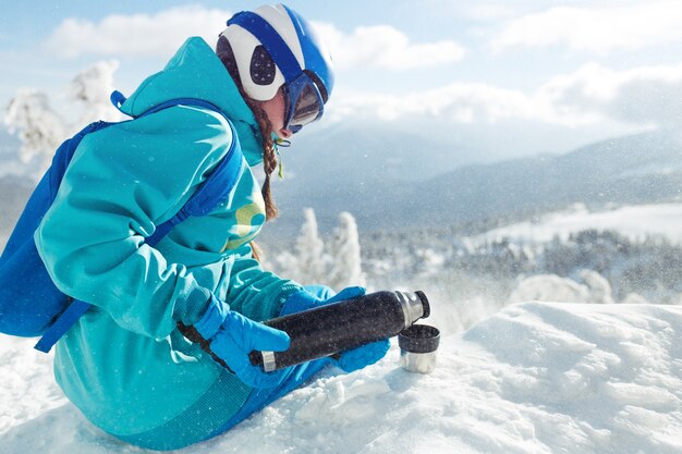 Hermosa mujer en ropa de invierno bebiendo té en las montañas. Concepto de viaje, ocio, libertad, deporte.