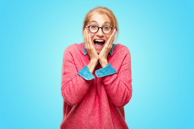 Hermosa mujer rubia adulta con una expresión sorprendida feliz, ojos abiertos de par en par y sonrisa amplia, asimiento