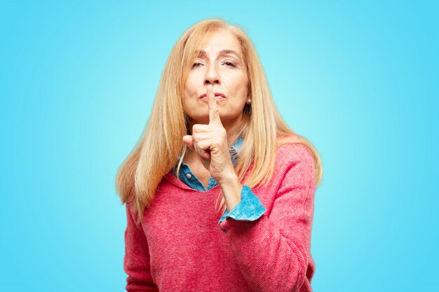 Hermosa mujer rubia adulta sonriendo, con el dedo índice delante de la boca, pidiendo silencio o sha