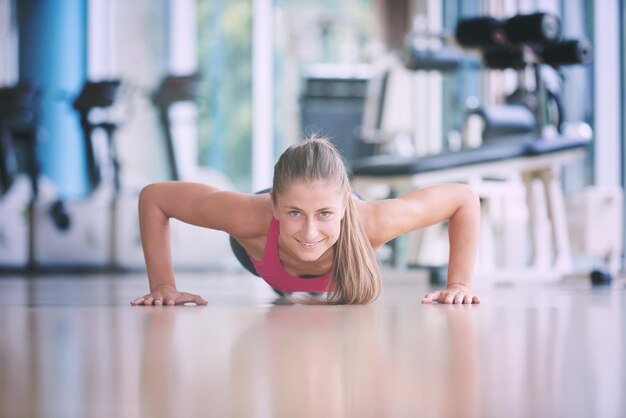 Hermosa mujer rubia calentando y haciendo flexiones en el gimnasio