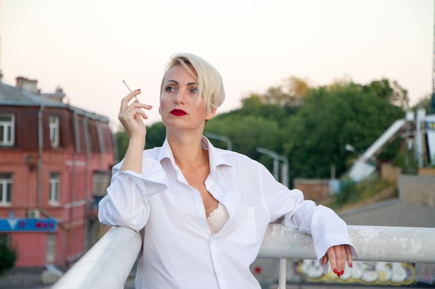 Hermosa mujer rubia en una camisa blanca fumando