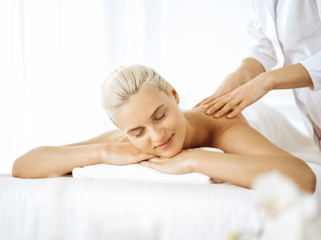 Hermosa mujer rubia disfrutando de un masaje de espalda con los ojos cerrados. Concepto de salón de spa.