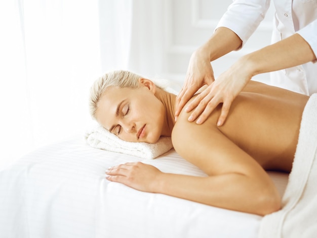 Hermosa mujer rubia disfrutando de un masaje de espalda con los ojos cerrados. Concepto de salón de spa.