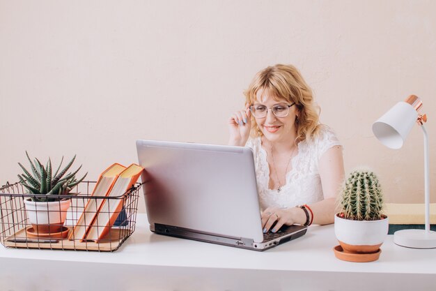 Una hermosa mujer rubia con gafas se sienta en una computadora portátil y trabaja