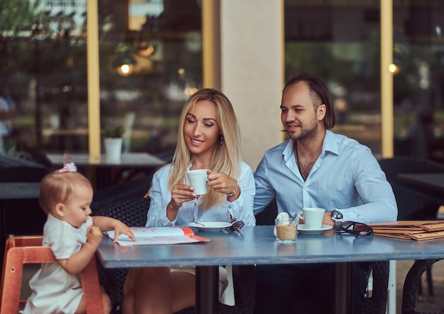 Hermosa mujer rubia y hombre guapo durante el tiempo con su pequeña hija en un café al aire libre. Concepto de familia y personas.