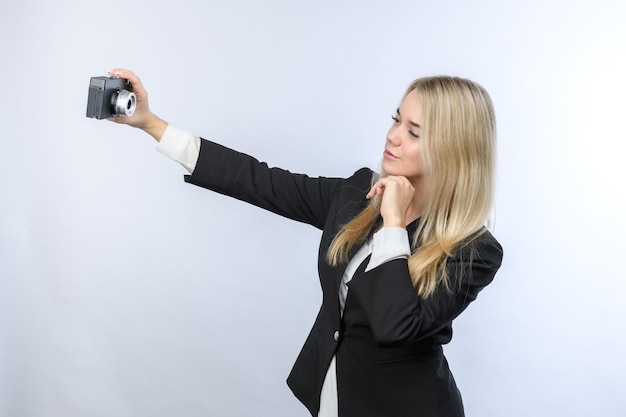 Hermosa mujer rubia joven haciendo selfie por cámara retro sobre fondo blanco.