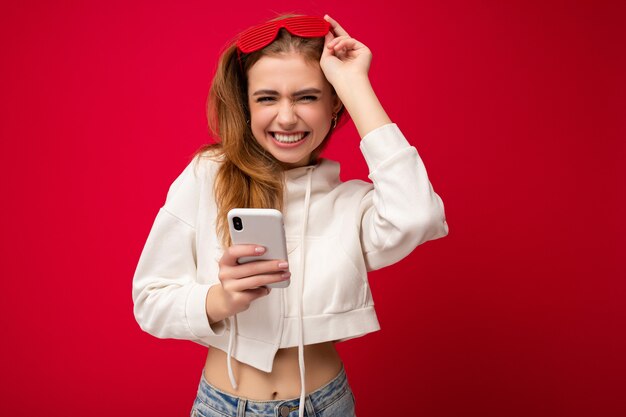 Hermosa mujer rubia joven positiva emocional con elegante sudadera con capucha blanca y colorido divertido