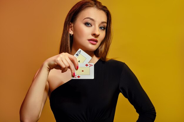 Hermosa mujer rubia con maquillaje brillante manicura roja en vestido negro está mostrando dos ases posando sobre fondo colorido Casino de póquer de entretenimiento de juego Primer plano