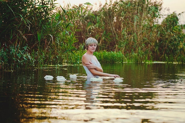 Hermosa mujer rubia con pelo corto nadando, relajándose en el lago al atardecer. Vacaciones de verano.