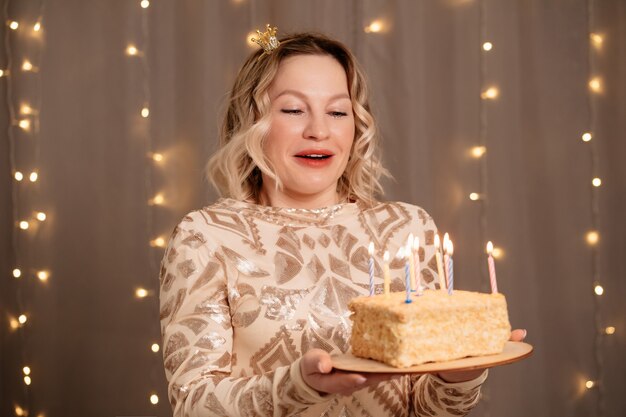 Hermosa mujer rubia en una pequeña corona en la cabeza con un pastel de cumpleaños y velas.