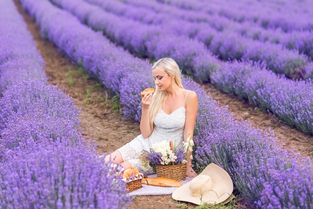 Hermosa mujer rubia en un picnic en un campo de lavanda.