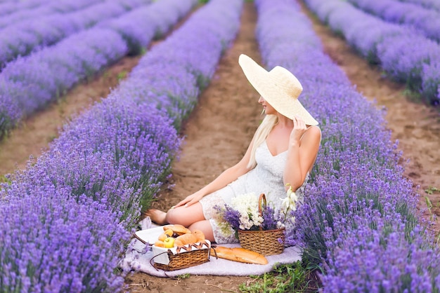 Hermosa mujer rubia en un picnic en un campo de lavanda.