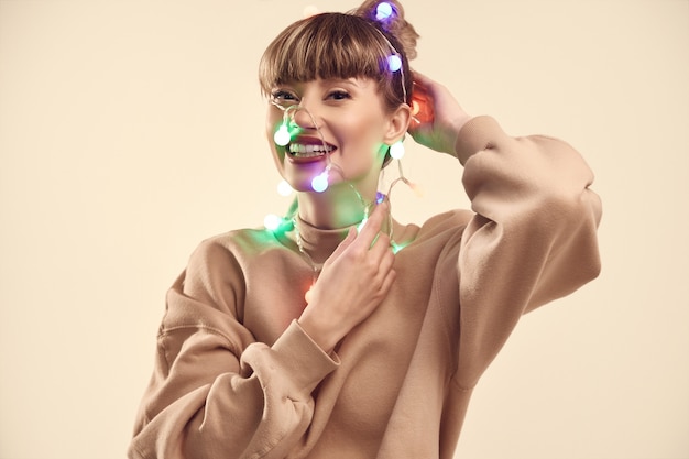 Hermosa mujer rubia positiva con luces de navidad en la cabeza